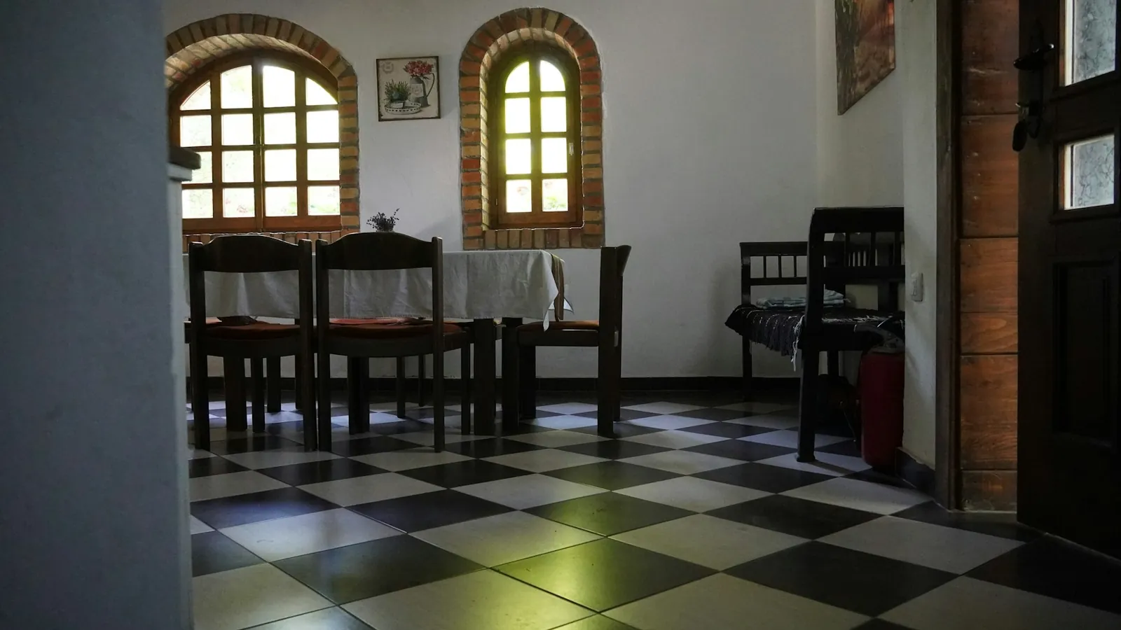 Sala de refeições de uma pousada, com mesa, cadeiras e piso xadrez