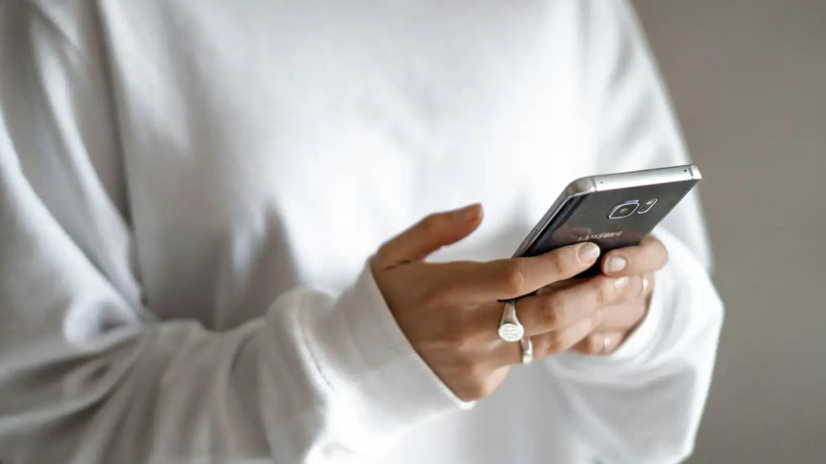 Pessoa de blusa branca segurando o celular com as duas mãos