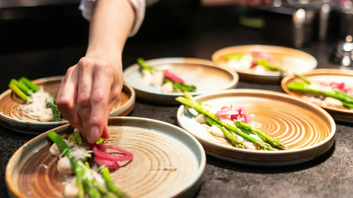 Cozinheira finalizando pratos com aspargos na cozinha de um restaurante