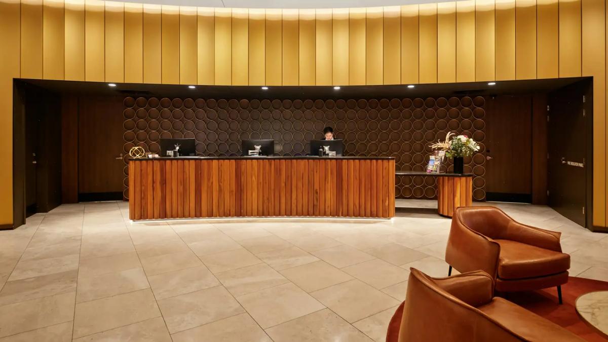 Balcão de madeira da recepção de um hotel, com poltronas de couro no saguão